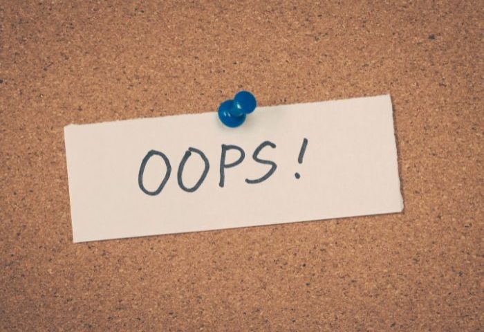 A white piece of paper with "OOPS!" written on it is pinned to a corkboard with a blue pushpin.